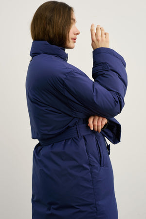 A model showcases a stylish navy blue MEOTINE puffer coat with a belted waist, highlighting its modern design and comfort.