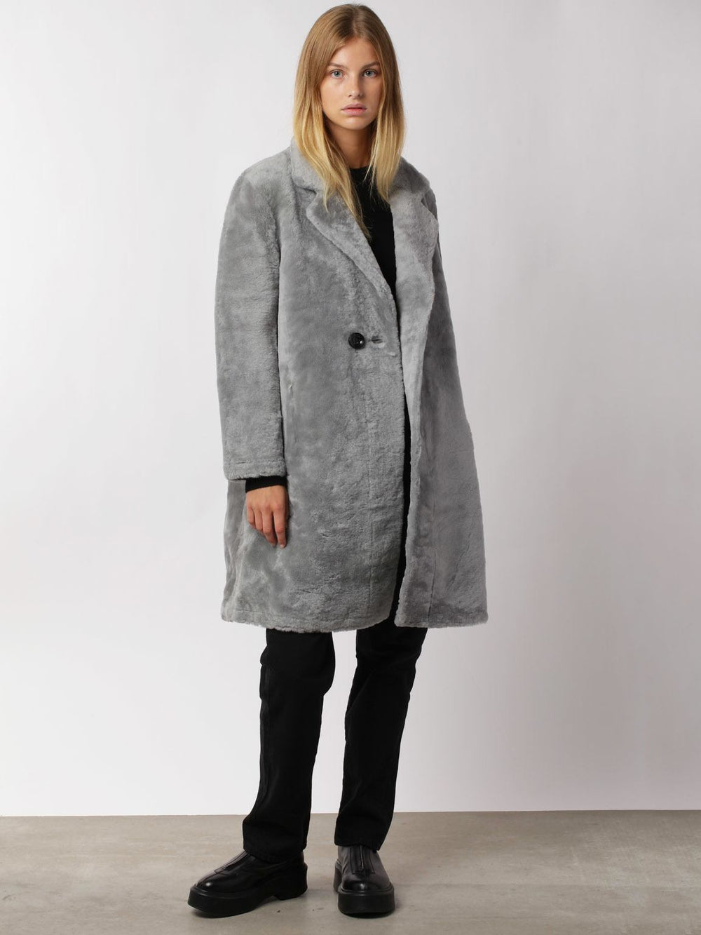 A model wears a stylish gray faux fur coat by MEOTINE, paired with black pants and shoes, set against a neutral background.