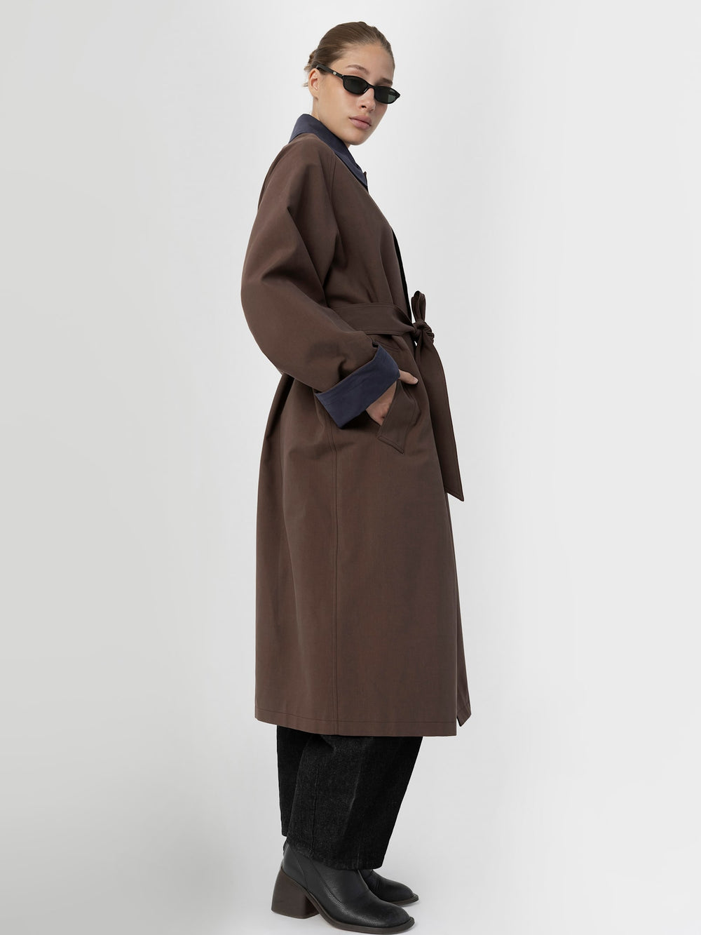 A model wears a stylish oversized brown coat with navy collar and cuffs, paired with a gray top and black pants. MEOTINE.