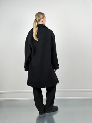 A model wearing a black oversized coat from MEOTINE, styled with loose black pants, viewed from the back against a neutral backdrop.