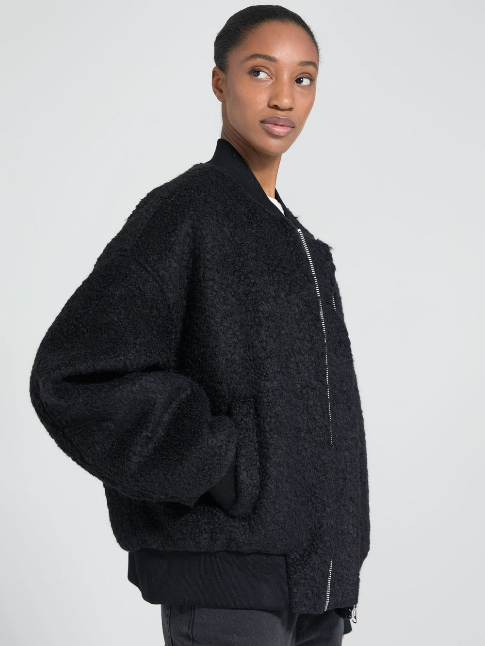 A model showcases a cozy black bomber jacket with a plush texture, featuring a zip closure and oversized sleeves by MEOTINE.