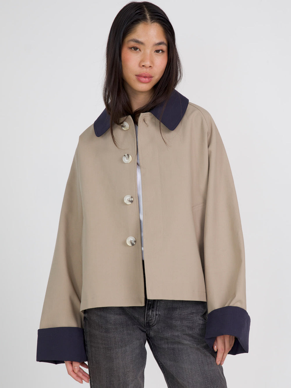 A model showcases a stylish beige jacket with a large collar and navy cuffs, featuring prominent buttons. MEOTINE's chic design stands out.