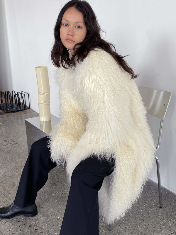 A model sits on a chair wearing a fluffy white MEOTINE sweater paired with black pants, showcasing a cozy and stylish look.