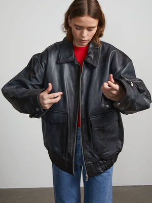 A model wears a stylish oversized black leather jacket from MEOTINE, paired with a red top and blue jeans, showcasing a modern look.