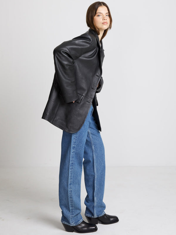 A model showcases a stylish black leather jacket paired with loose blue jeans and chunky black boots, embodying MEOTINE's chic aesthetic.